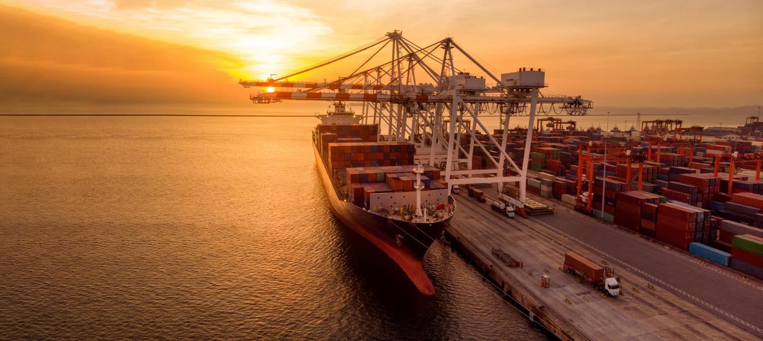 Container ship berthed at a port with cranes at sunset